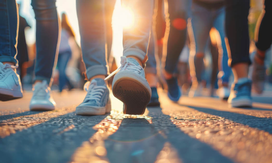 Closeup, shoes and group in street, walking and sunshine with lens flare, cooperation and protest. March, feet and people in city, tar road and summer with action for justice, forward and outdoor.