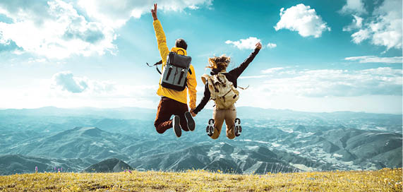 Hikers with backpacks jumping with arms up on top of a mountain - Couple of young happy travelers climbing the peak - Family, travel and adventure concept